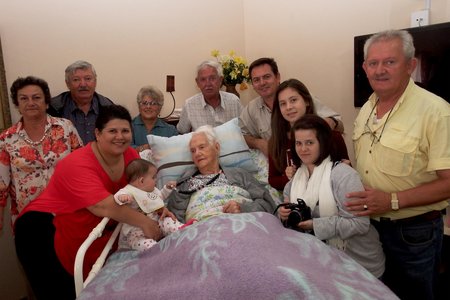 Kinders, kleinkinders, agter-kleinkinders en agter-agter-kleinkind staan bankvas agter Tannie Rens Fourie tydens haar verjaardag